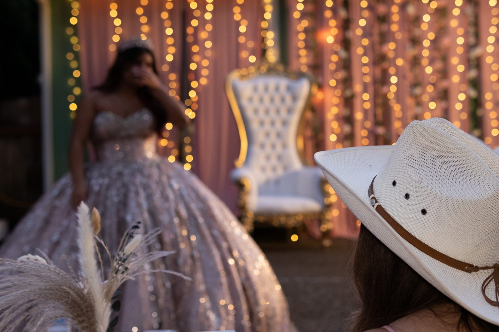 Guest in a white cowboy hat watching a quinceañera under string lights