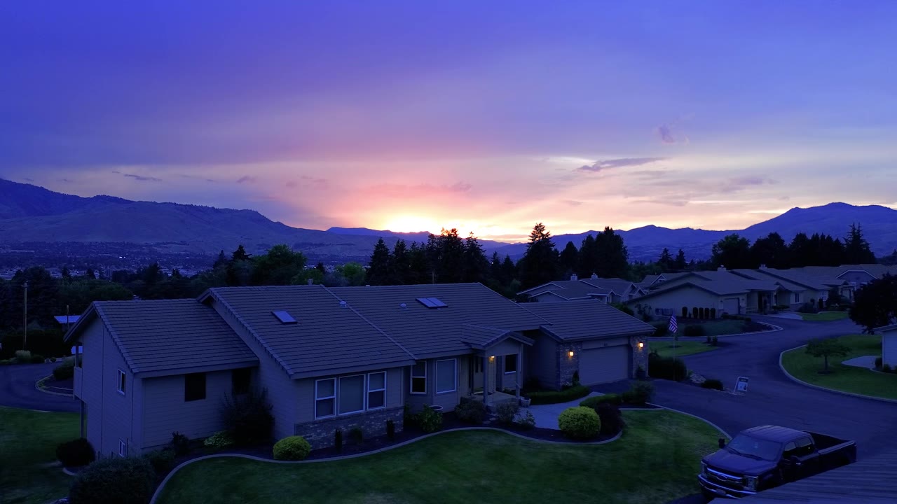 Aerial twilight view of a home with its lights on at sunset